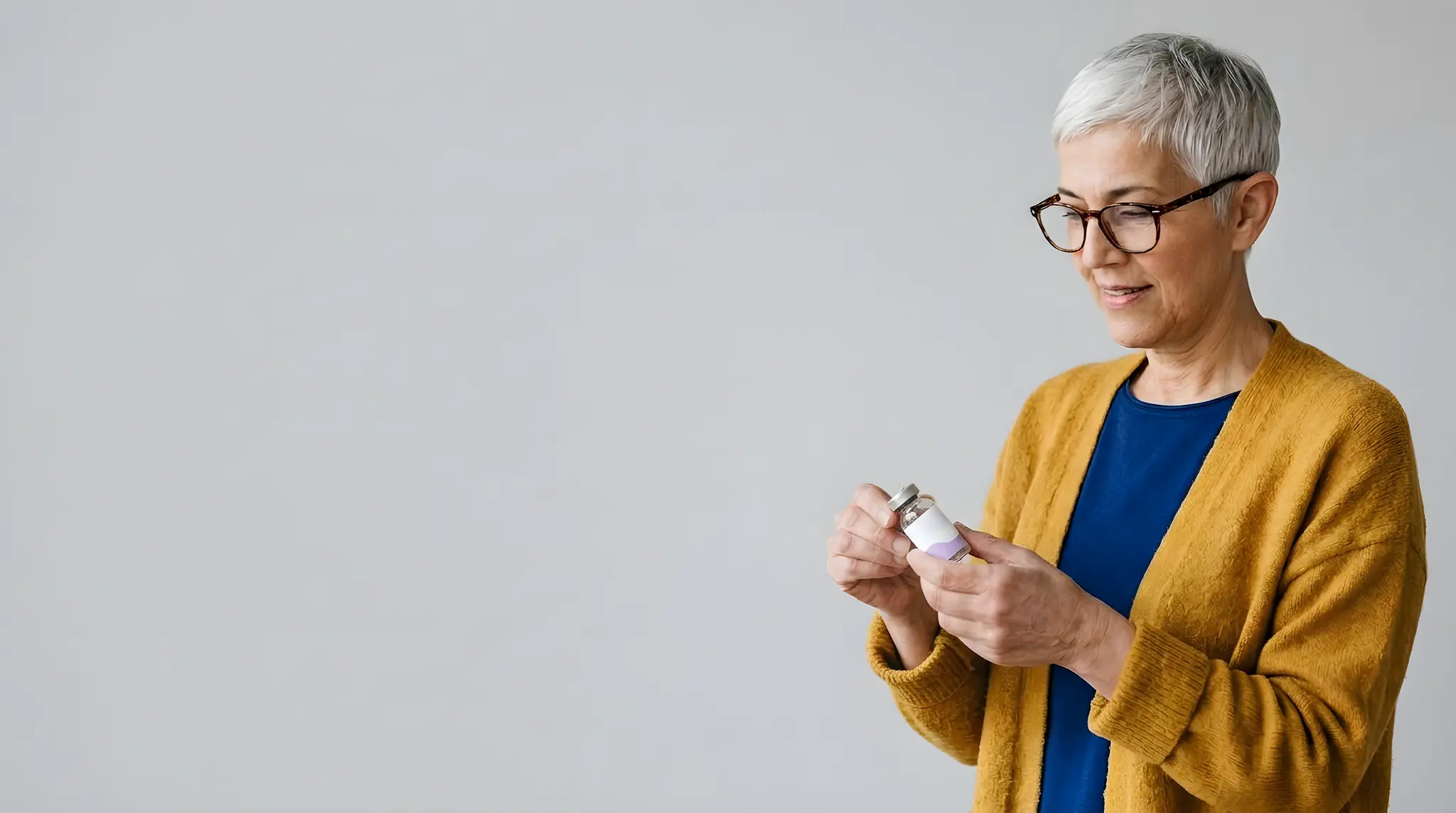 Pharmacist in a mustard cardigan holding a medication vial